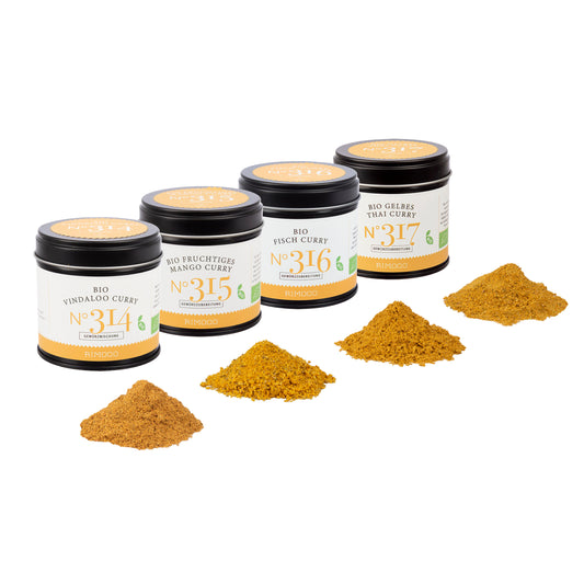 Vier Gläser Bio Curry Gewürz-Set N°2, davor passendes Häufchen gemahlenes Currypulver.
