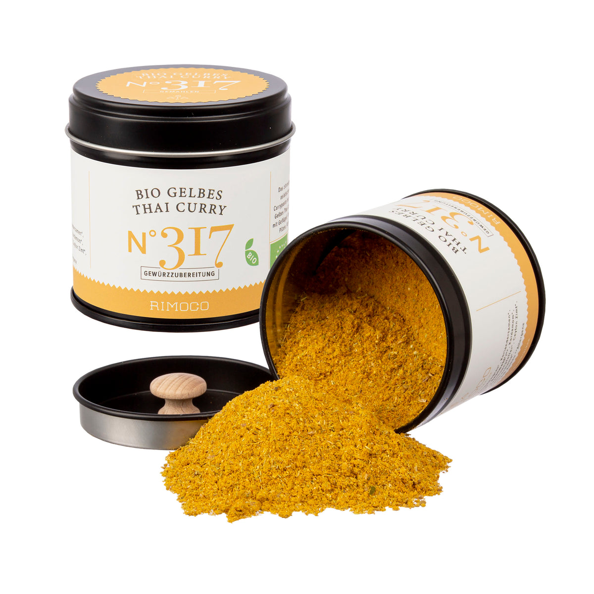 Zwei Dosen Bio Curry Gewürz-Set N°2, eine umgekippt mit verstreutem Pulver und einem Gewürzlöffel.