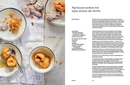 Drei Schalen Aprikosensorbet mit Löffeln auf Marmor, Gebäckstücke daneben.
