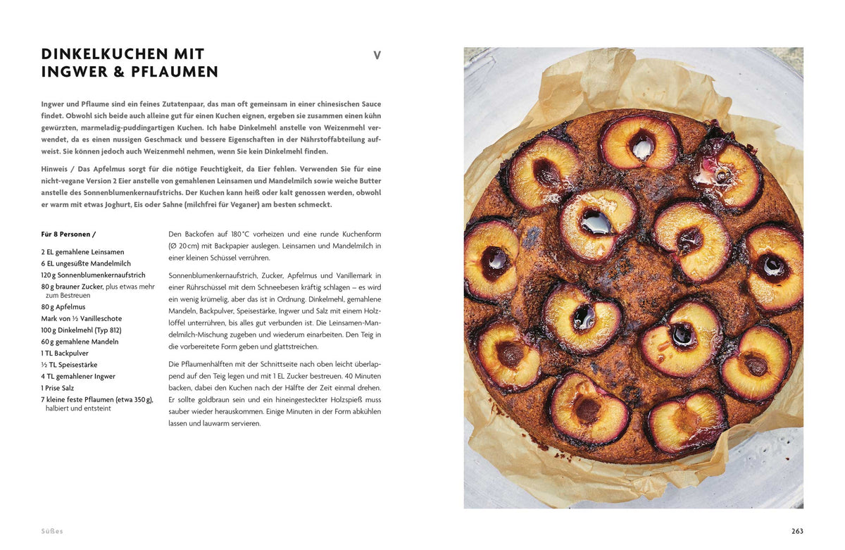 Ein runder Zwetschgenkuchen mit Ingwer liegt auf Backpapier neben dem Buch Asien vegetarisch.