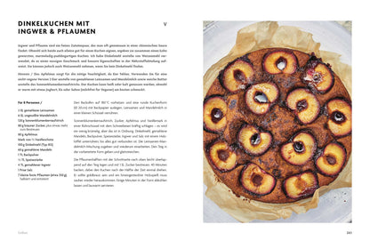 Ein runder Zwetschgenkuchen mit Ingwer liegt auf Backpapier neben dem Buch Asien vegetarisch.