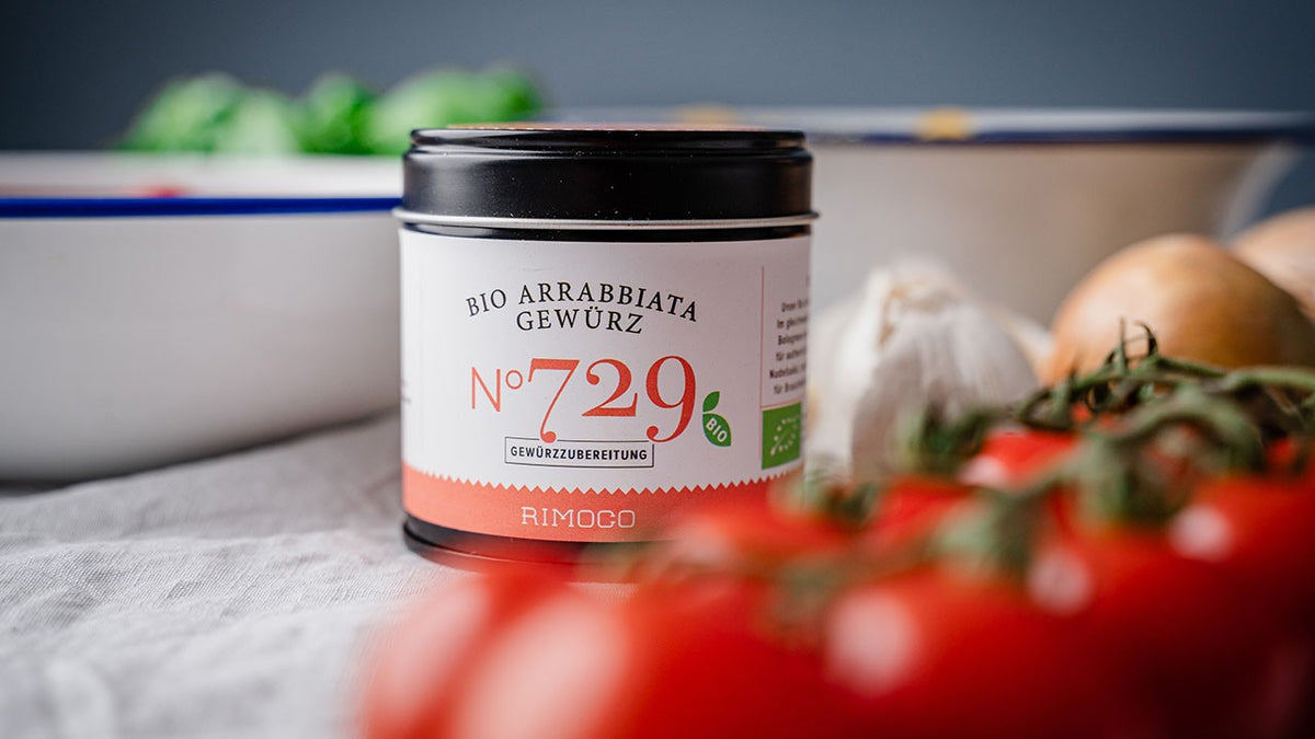 Bio-Arrabbiata-Gewürzdose zwischen frischen Tomaten, Knoblauch und Zwiebeln.