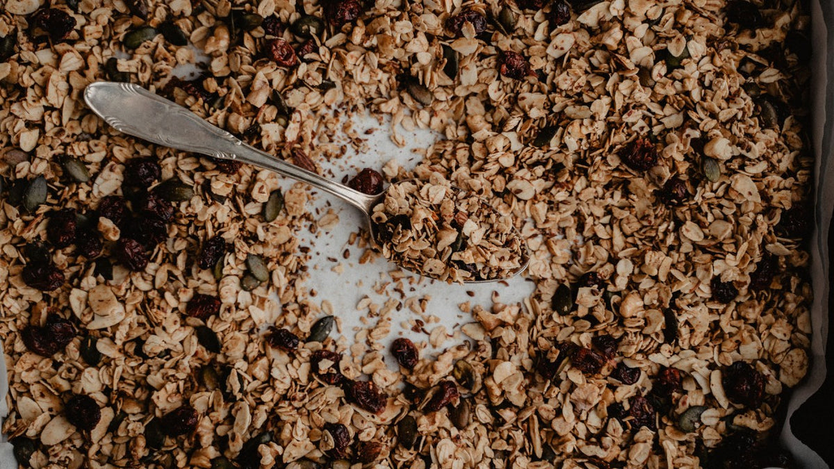 In einer Schale mit goldbraunem Granola, Haferflocken, Samen und getrockneten Cranberries liegt ein Löffel.