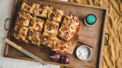 Geschnittene Focaccia mit Tomaten, Zwiebeln und SalMartins Meersalz auf einem Holztablett.