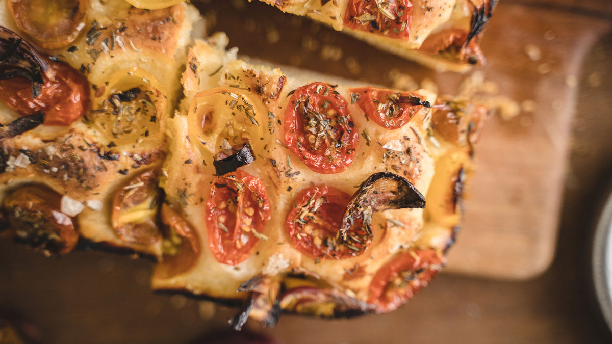 Nahaufnahme von Focaccia mit Tomaten, frischen Kräutern und grobem Meersalz.
