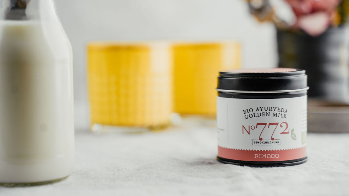 Bio Ayurveda Golden Milk Nr. 772 neben einer Glasflasche und gelben Bechern auf dem Tisch.
