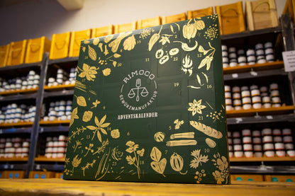 Bio Gewürz Adventskalender in Grün mit goldenen Illustrationen, steht im Regal eines Gewürzladens.