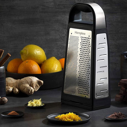 Microplane Turmreibe Elite Box – Reibe auf einem Tisch mit Zitrusfrüchten, Ingwer, Gewürzen und geriebenem Gemüse.
