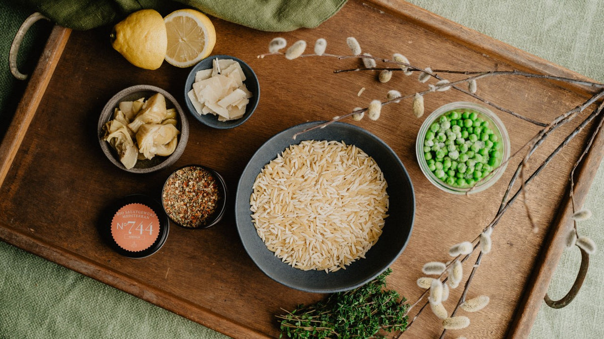 Tablett mit Orzo, grünen Erbsen, Artischocken, Zitrone, Kräutern und Gewürzen in Schalen und lose.