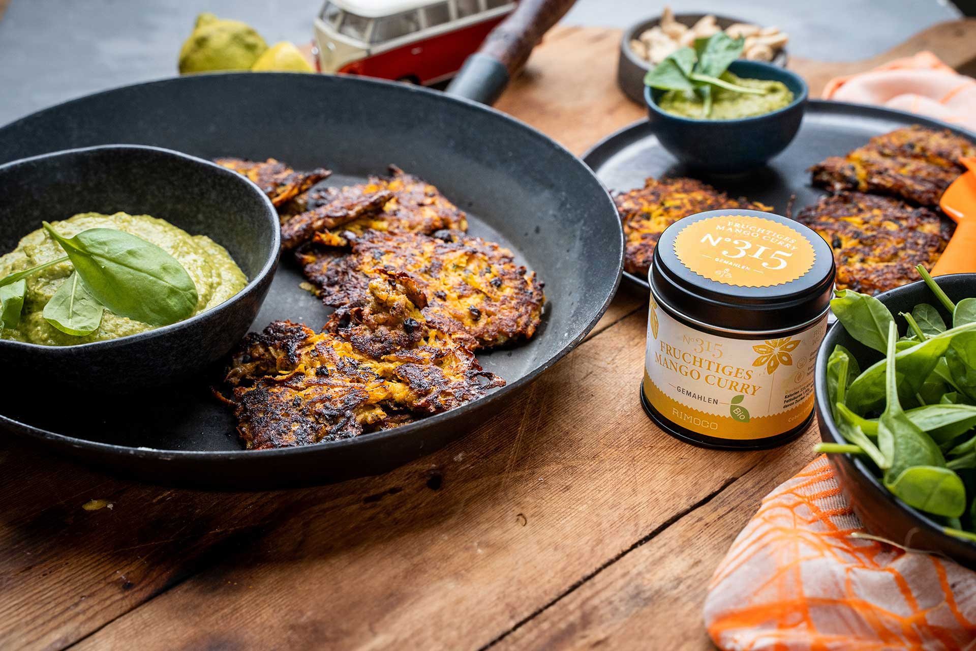 In einer Pfanne gebratene Bratlinge mit grüner Sauce, einer Dose Curry und frischem Spinat auf einem Holztisch.
