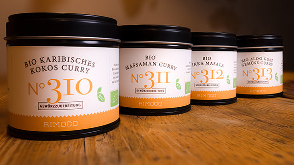 Vier Dosen Bio Curry Gewürz-Set N°1, darunter Karibisches Kokos Curry, auf Holzoberfläche.