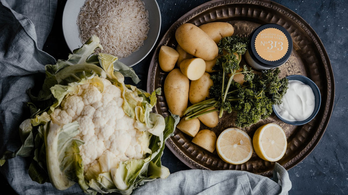 Blumenkohl, Kartoffeln, Petersilie, Zitrone, Reis, Joghurt und gemahlene Gewürze auf einem Teller.