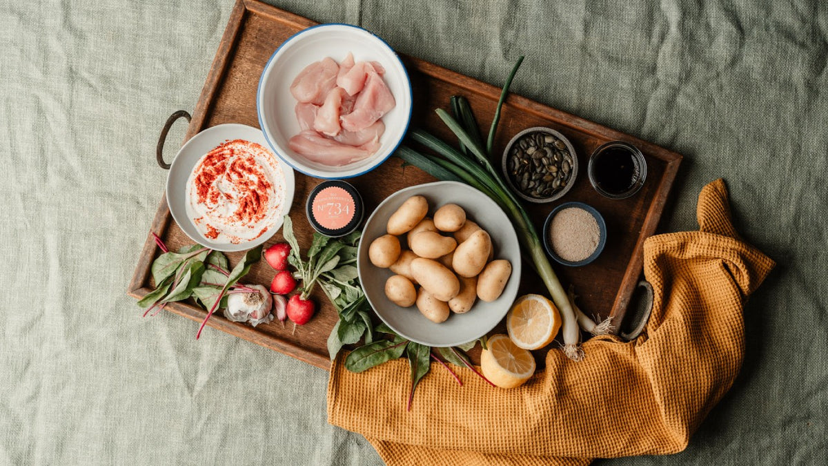 Ein Tablett mit rohem Hähnchenfleisch, Kartoffeln, Radieschen, Gewürzen und frischen Frühlingszwiebeln mit Zitrone.