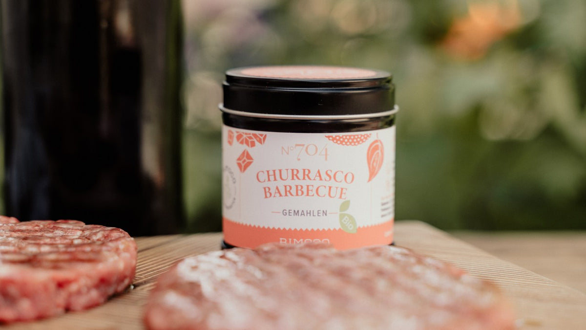 Churrasco-Barbecue-Gewürz im Glas auf einem Holzbrett neben frischen Burger-Patties.