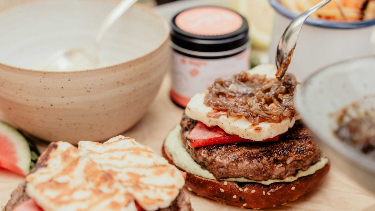 Ein Burger mit Käse, Tomate und karamellisierten Zwiebeln liegt auf einem Brötchen neben Pommes.