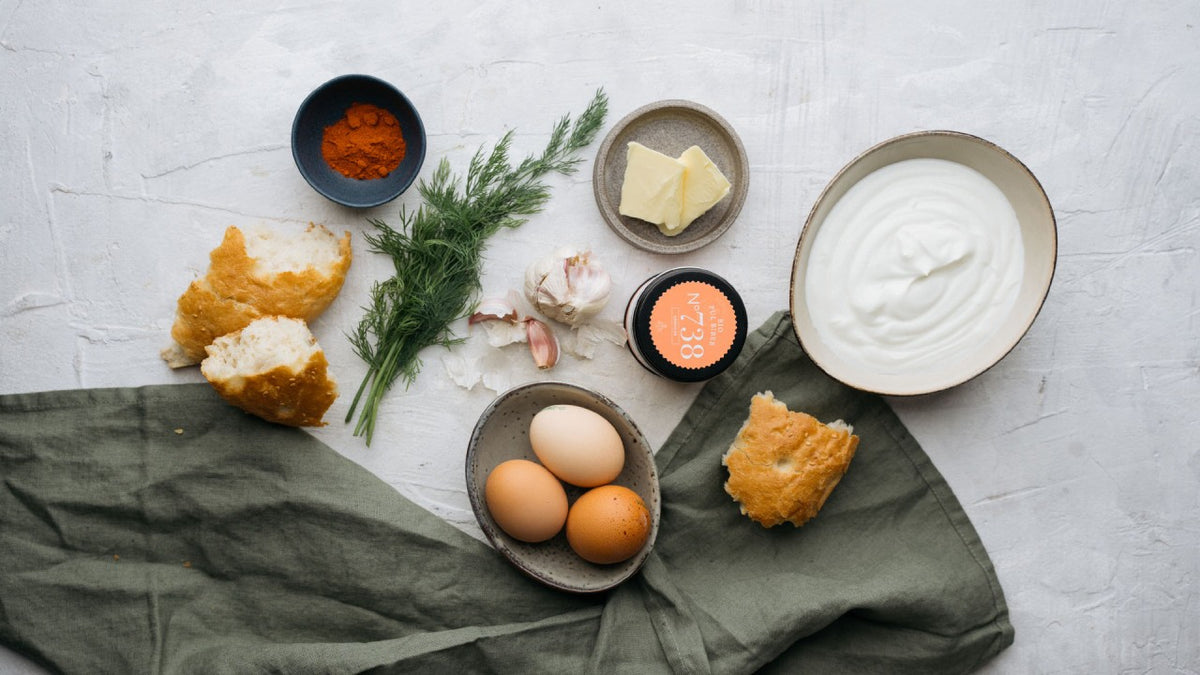 Eier, Joghurt, Butter, frischer Dill und gemahlener Paprika auf einem grünen Tuch auf einer hellen Fläche.