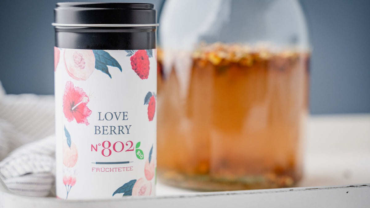 Stellen Sie „Love Berry No 802“ neben ein Glas mit beerigem Früchtetee auf ein Tablett.