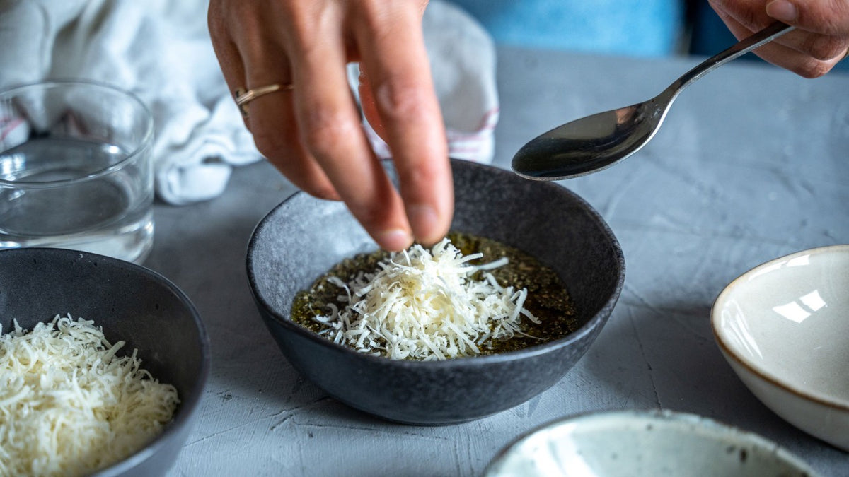 Eine Hand streut geriebenen Käse über eine dampfende Suppe und hält einen Löffel darüber.