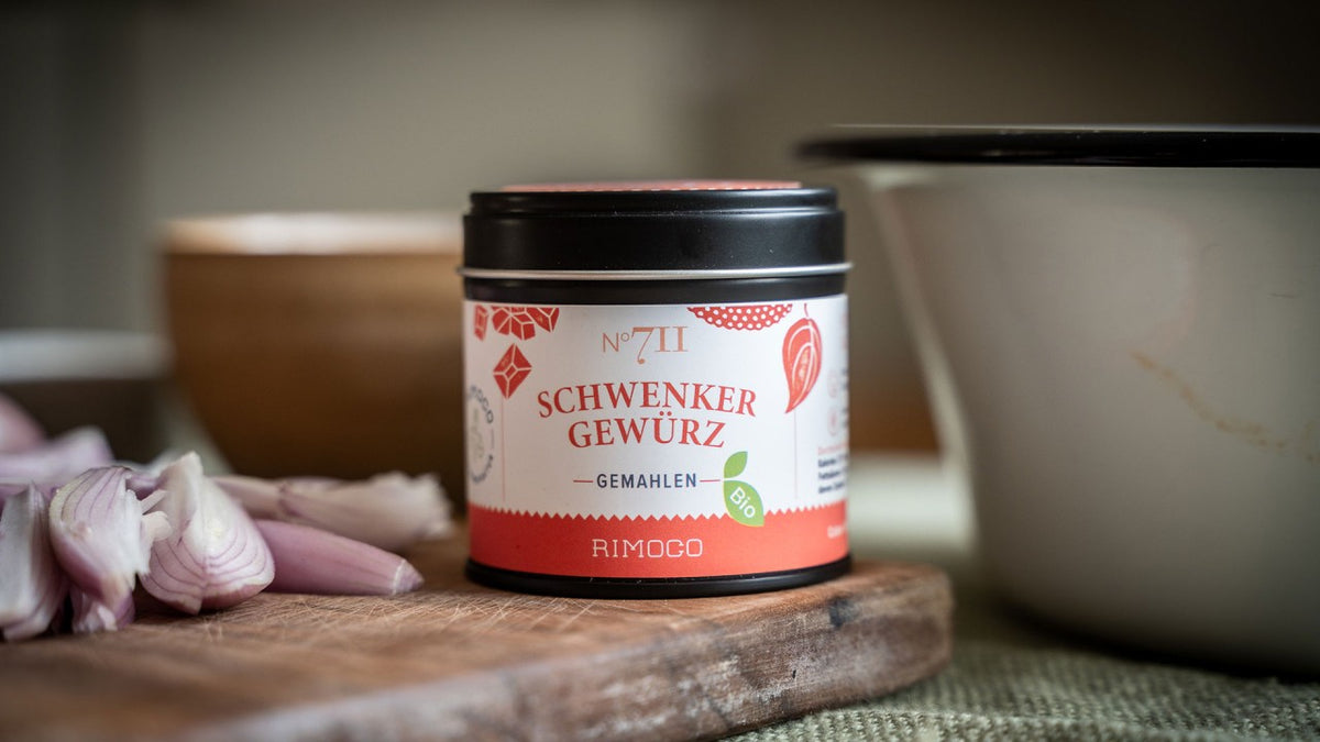 Eine Schwenker-Gewürzdose auf einem Tisch neben geschnittenen Schalotten und einer weißen Schale.