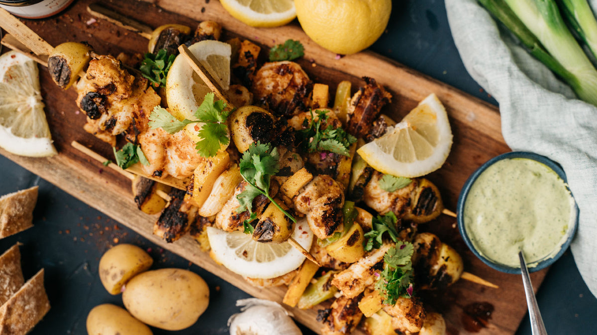 Gegrillte Hähnchenspieße mit Zitronenstücken, frischen Kräutern und Gewürzset Ottolenghi Simple.