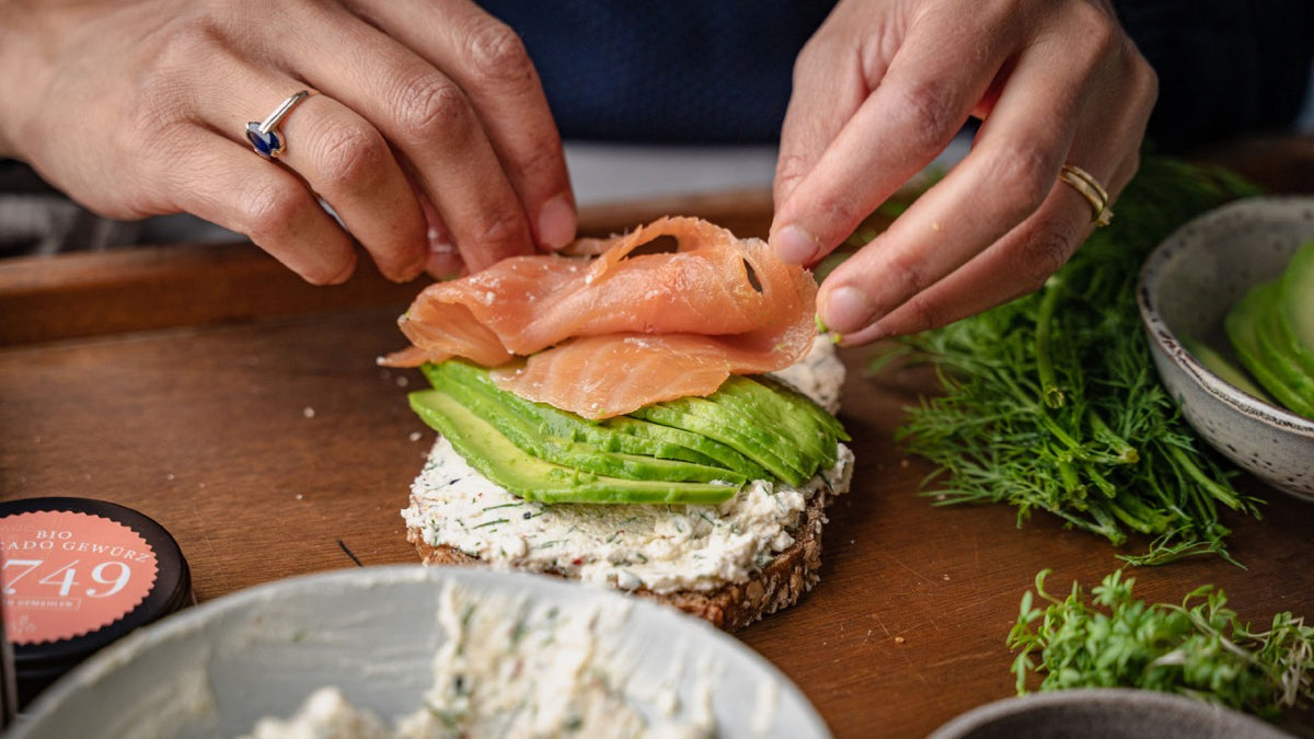 Räucherlachs auf Toast mit Frischkäse, Avocado und frischen Kräutern.