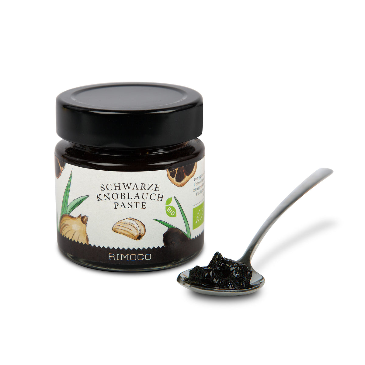Glas mit Aufschrift Bio Schwarze Knoblauchpaste und ein Löffel schwarze Paste daneben.