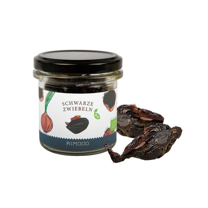 Bio Schwarze Zwiebeln fermentiertes Glas und zwei schwarze fermentierte Zwiebeln auf weißem Hintergrund.