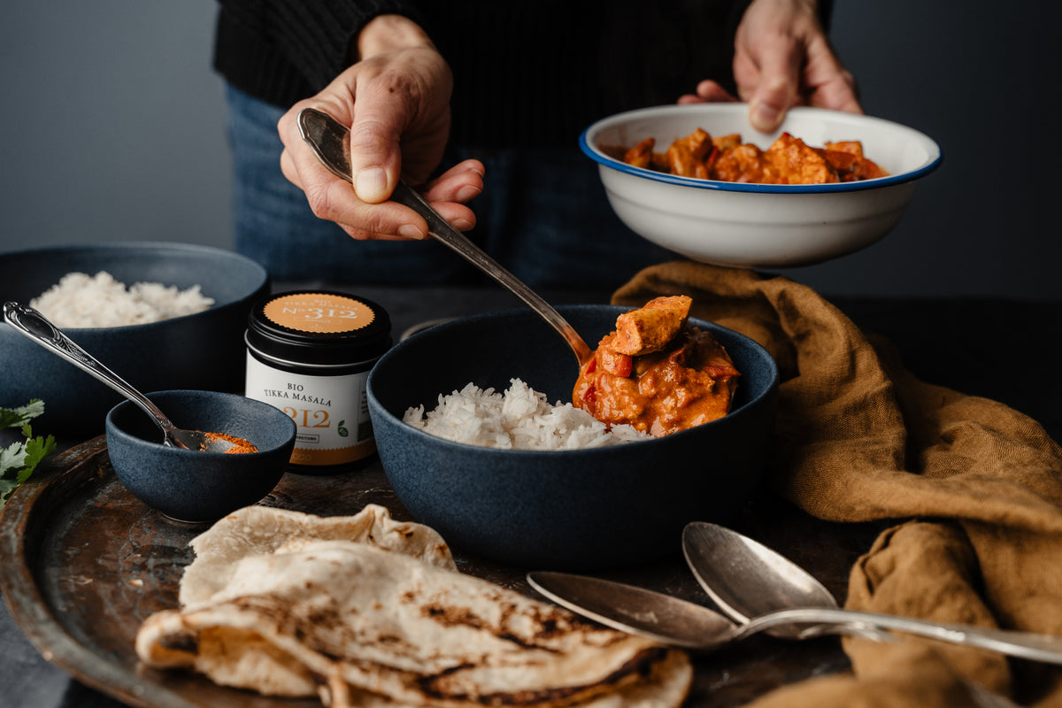 Tikka Masala mit Reis und Naan wird serviert, daneben das Gewürzseminar Indien und bunte Rezepte.