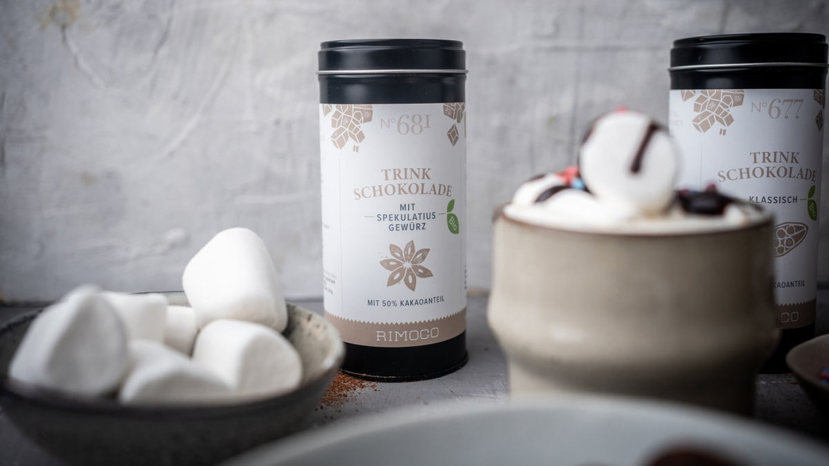 Trinkschokolade mit Marshmallows und eine Tasse heiße Schokolade im Vordergrund.