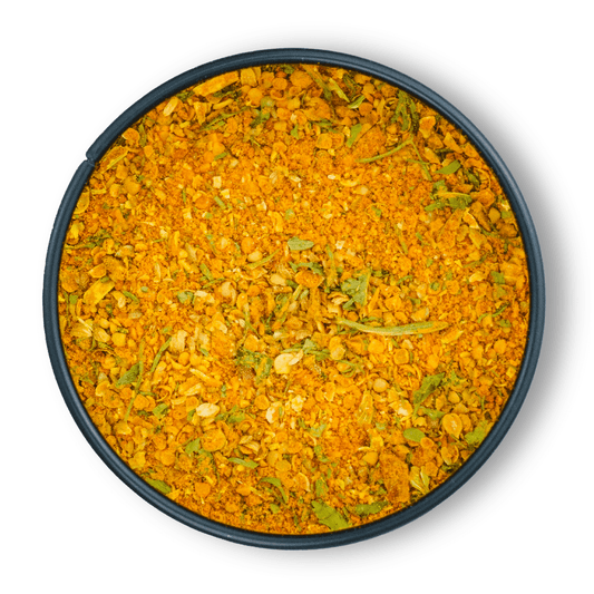 Ein rundes dunkles Gefäß mit Bio Aloo Gobi Gemüsecurry in Orange-Gelb und grünen Kräutern.