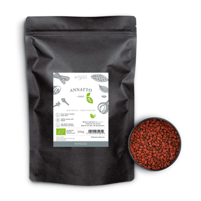 Schwarzer Bio Annatto Beutel neben einer Schale mit kleinen roten Annattosamen.