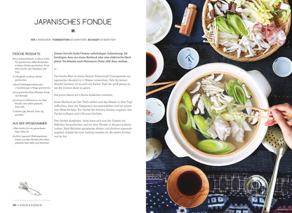 Eine Hand taucht Essen in den Authentisch Japanisch-Topf, umgeben von frischem Gemüse und Saucen.