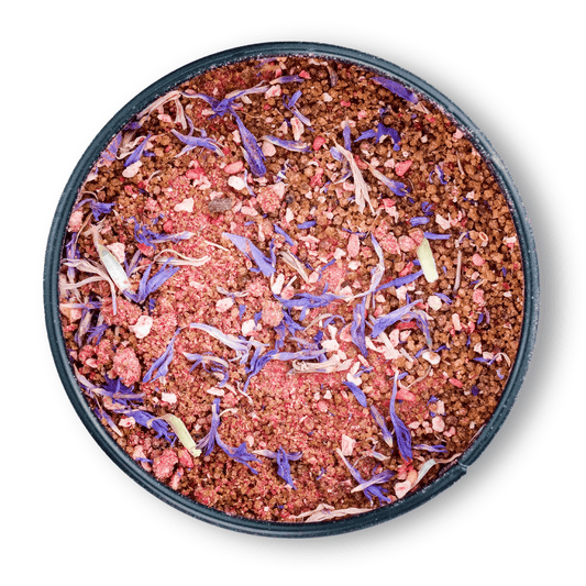 Bio Ayurveda Früchtetraum: Runddose mit rosa Fruchtpulver, darauf lila Blütenblätter.