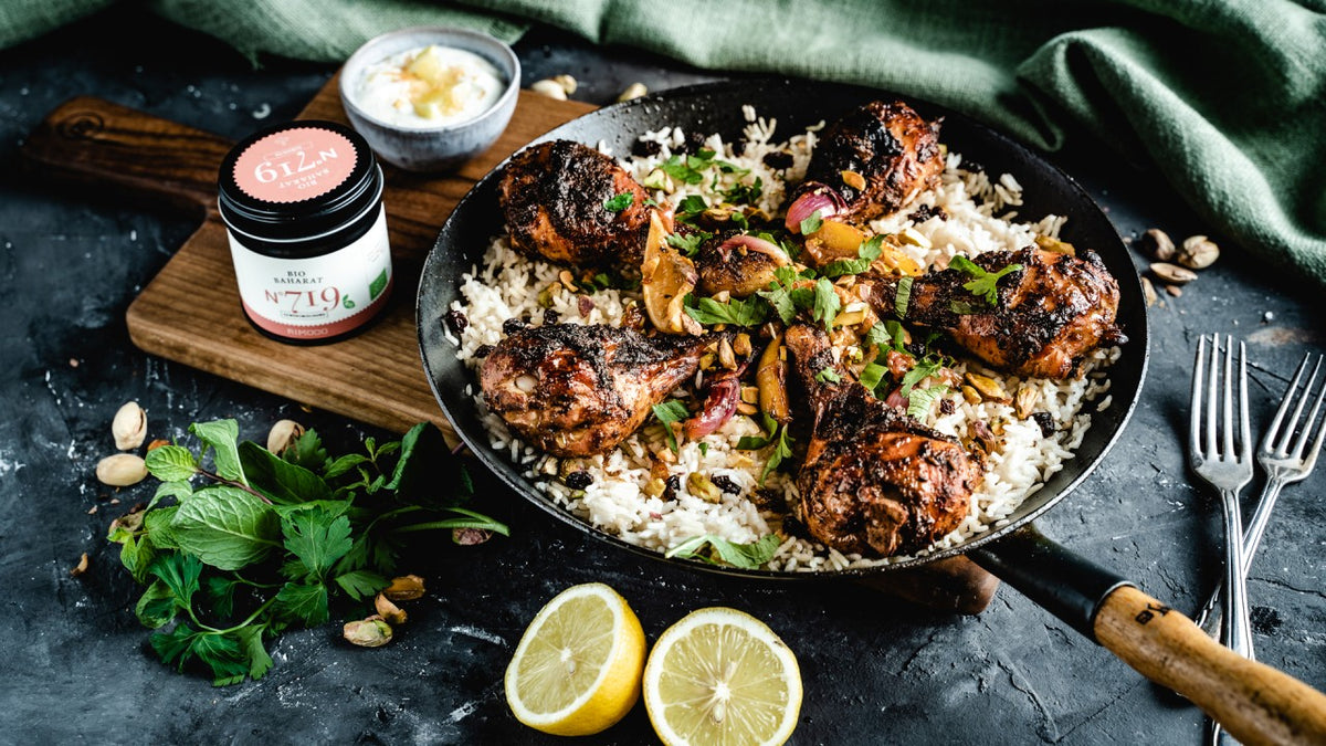 Pfanne mit gewürztem Hähnchen und Safranreis, garniert mit Kräutern, dazu Zitronen, Joghurt und Minze.