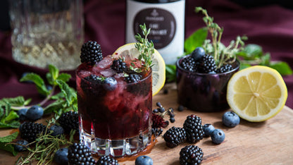 Zwei Cocktails mit Die Antwort BIO Gin, Beeren, Zitrone und Kräutern auf Eis auf einem Holzbrett.
