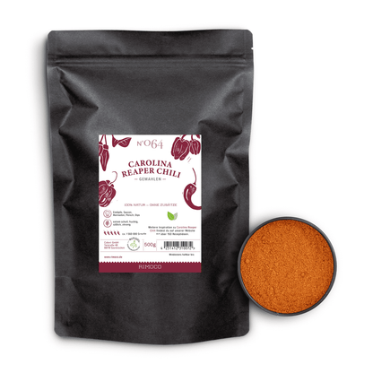 Schwarzer Beutel mit Aufschrift Carolina Reaper Chili neben einer Schale mit scharfem, orangem Chilipulver.