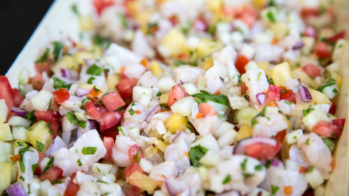 Nahaufnahme von Ceviche mit Fischwürfeln, Tomaten, Zwiebeln, Koriander und bunten Paprikaschoten.