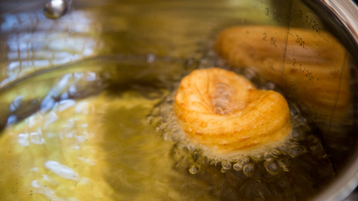 Ein Donut brät in heißem Öl in einem Metalltopf, an der goldbraunen Oberfläche bilden sich Blasen.