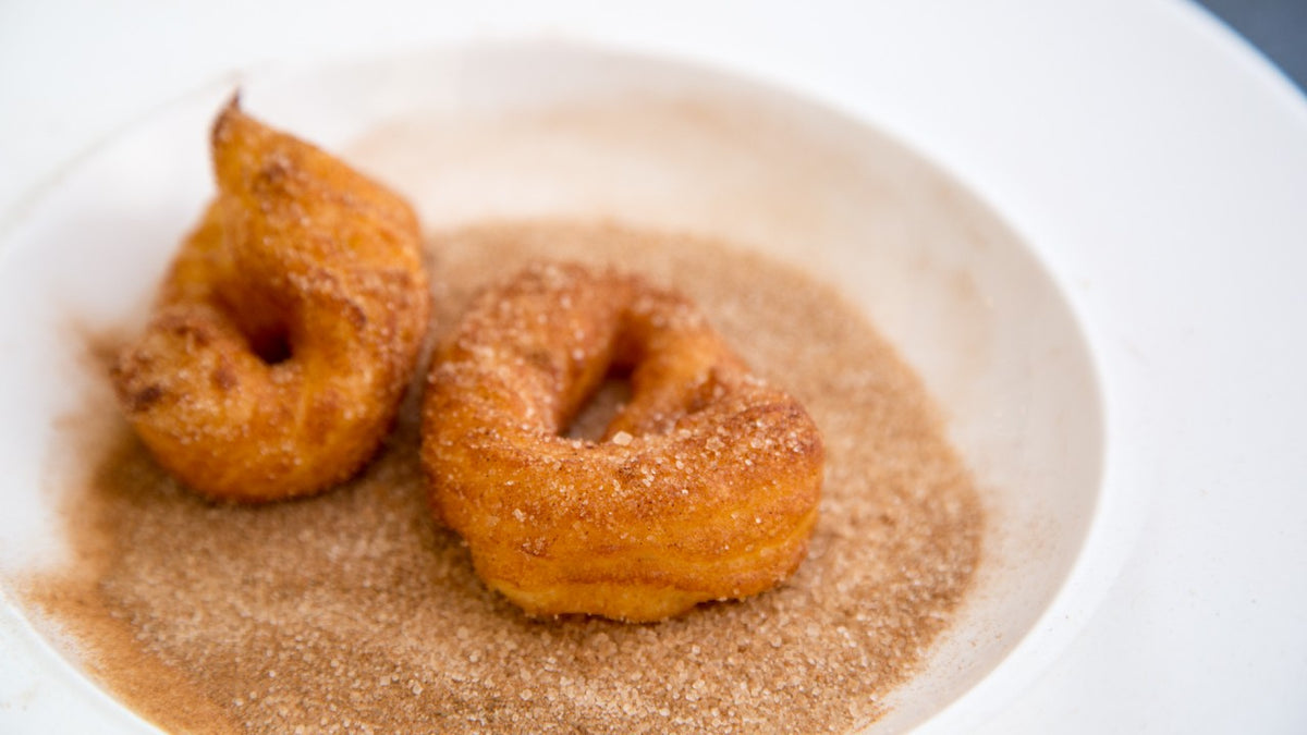 Zwei frisch gebackene Churro-Twists mit Zimt und Zucker liegen auf einem weißen Teller.
