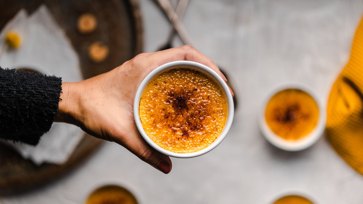 Crème brûlée mit karamellisierter Zuckerschicht in einer Schale, von oben, aus der Hand fotografiert.