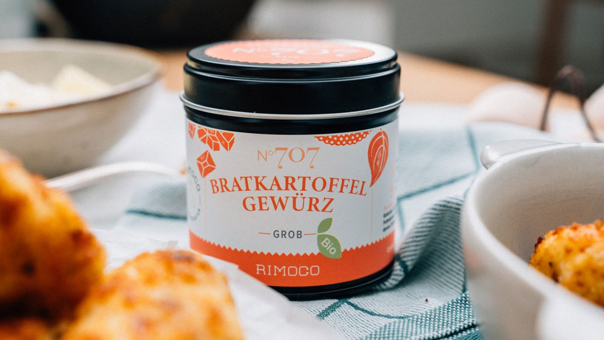 Eine Dose mit Bratkartoffelgewürz steht auf einem Tisch neben einem Teller mit Essen.