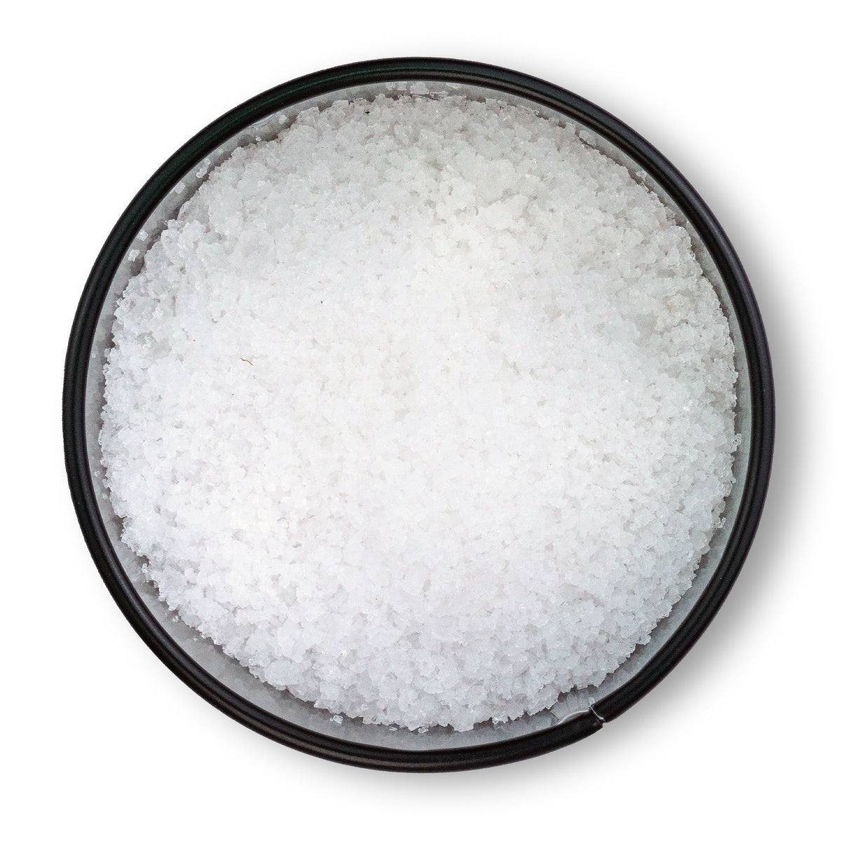 Runde schwarze Schale mit grobem Fleur de Sel de Camargue von oben auf weißem Hintergrund.