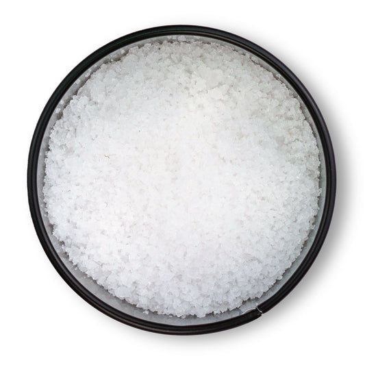 Runde schwarze Schale mit grobem Fleur de Sel de Camargue von oben auf weißem Hintergrund.