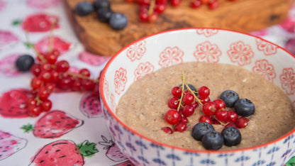 Schale Porridge mit Blaubeeren, roten Johannisbeeren und gemahlenem Ceylon-Zimt & Honig auf Erdbeertuch.