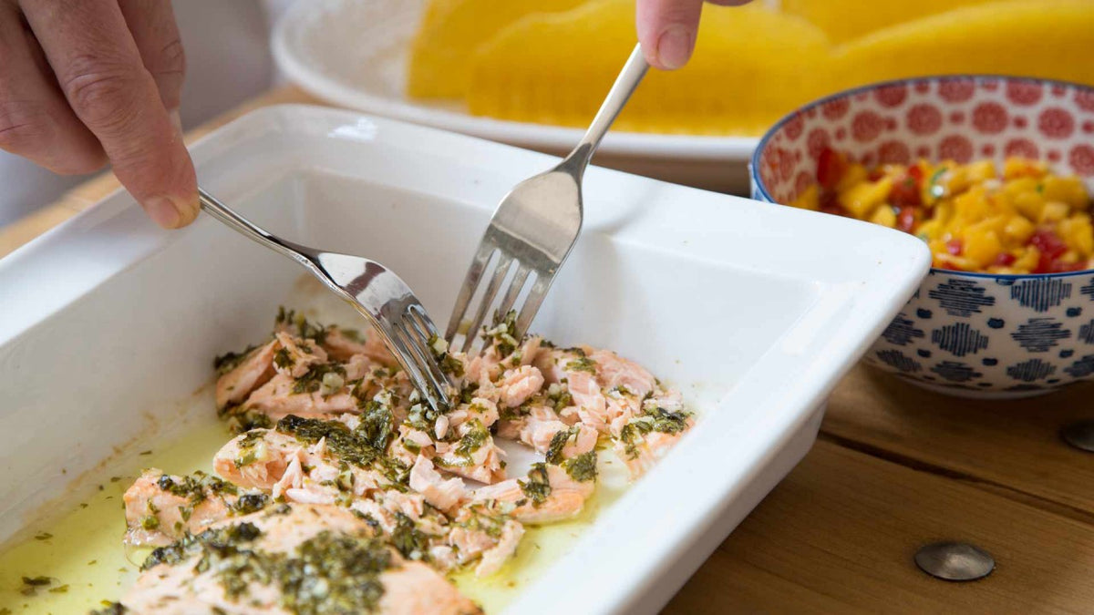 Gebratener Lachs mit Kräutern wird in einer weißen Schale portioniert, dazu gibt es Mango-Salsa.