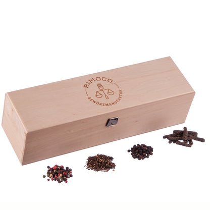 Holz-Gewürzbox mit Verschluss und Logo auf dem Deckel, davor vier Häufchen Tellicherry Pfeffer.