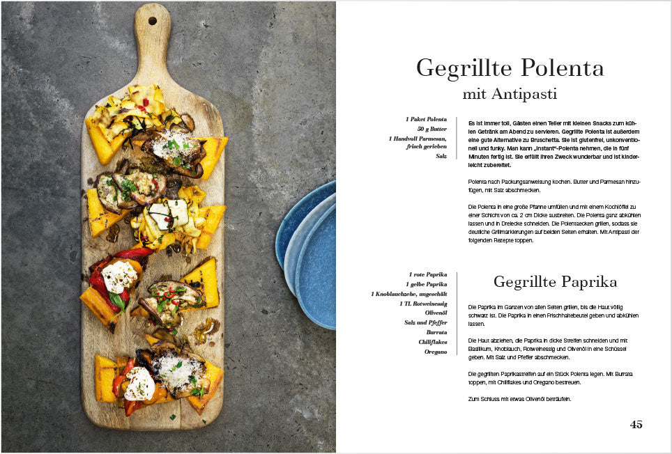 Gegrillte Polenta und Antipasti auf Holzbrett, daneben das Grillgemüse Kochbuch auf Deutsch.