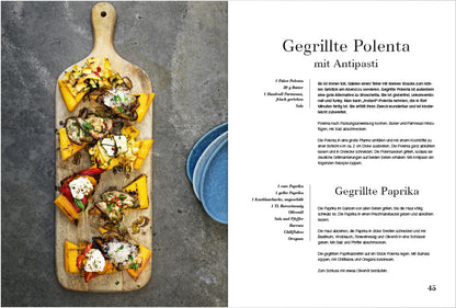 Polentascheiben mit Grillgemüse auf Holzbrett, daneben blaue Teller.