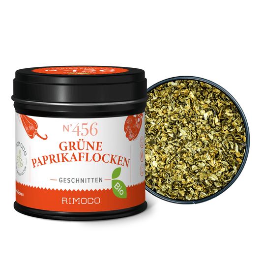 Bio Grüne Paprikaflocken in schwarzer Dose neben einer Schale, Paprika-Flocken sichtbar.