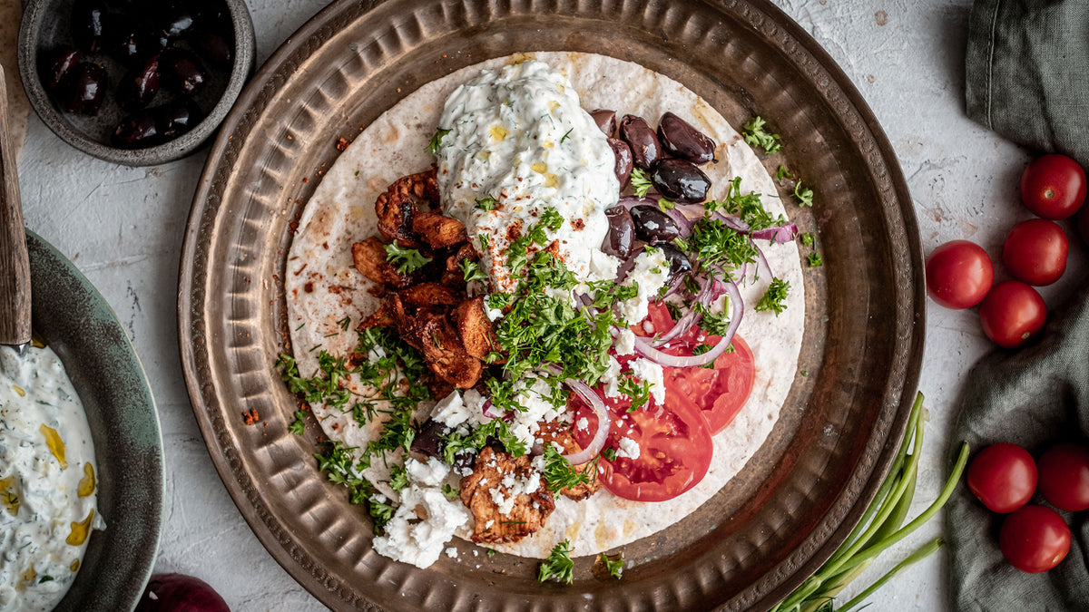 Pita mit Hähnchen, Tzatziki, Tomatenscheiben, Oliven, Petersilie und cremigem Feta-Käse.